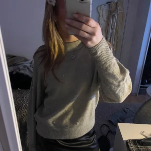 Grön/beige stickad tröja med pärlor - Säljer en mysig beigegrönaktig stickad tröja dekorerad med små pärlor. Tröjan har långa ärmar och ribbade muddar vid ärmslut och nederkant. Supergulligt med pärlorna!!!