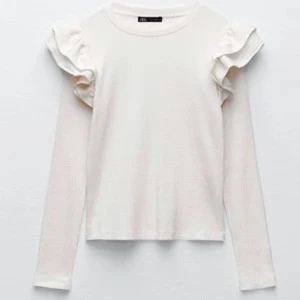 Vit långärmad topp från Zara - Säljer en stilren vit långärmad topp från Zara med volangdetaljer vid axlarna. Perfekt för en elegant och enkel look. Passar bra till både jeans och kjol.