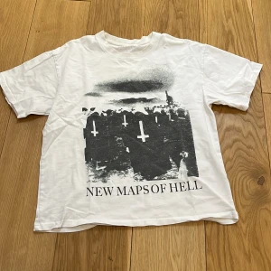 Playboycarti 'New Maps of Hell' t-shirt - Säljer en vit t-shirt med tryck 'New Maps of Hell' på framsidan och 'Whole Lotta Red Playboi Carti' på baksidan. T-shirten har korta ärmar och är i en normal passform. Perfekt för fans av Playboi Carti.