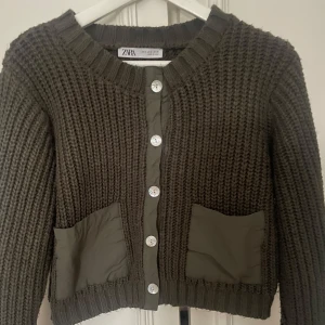Mgrön stickad kofta från Zara - Säljer en olivgrön stickad kofta från Zara med knappar framtill och två praktiska fickor. Koftan har en ribbad struktur och långa ärmar, perfekt för kyligare dagar. En stilren och bekväm tröja för alla tillfällen.