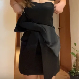 Svart axelbandslös klänning - Snygg svart axelbandslös klänning med en elegant knytning framtill. Perfekt för en stilren look. Klänningen är använd endast 1 gång och är i perfekt skick. Dragkedjan är lite seg men funkar ändå utmärkt! Storlek S