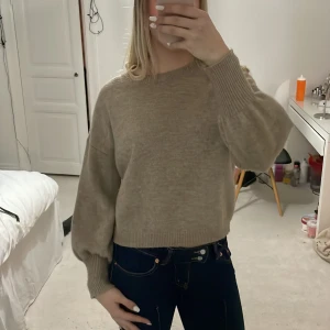 Beige stickad tröja - Säljer en mysig beige stickad tröja med långa ärmar och ribbade muddar. Perfekt för kyligare dagar och enkel att matcha med olika outfits. Passar både till jeans och kjol.