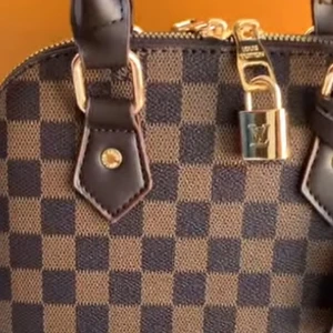 Rutig Lv handväska med bruna detaljer - Snygg Lv handväska med klassiskt rutigt mönster i brunt och svart. Väskan har en elegant design med dragkedja och guldfärgade detaljer. Perfekt för att ge din outfit en lyxig touch. Helt ny pris går att diskutera 