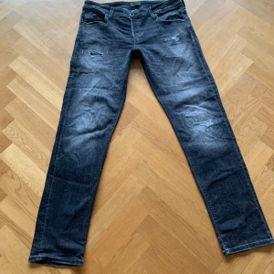 Svarta jeansbyxor från Jack & Jones - Snygga mörkgråa jeans från Jack n Jones. Slutningar på båda benen och slimfit. Använda lite men inga skador. W36. L34.
