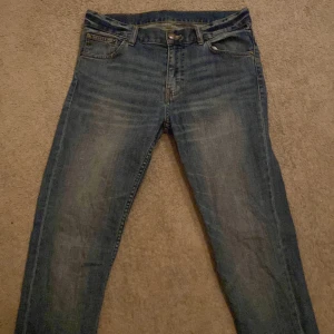 Blå jeans från Weekday - Snygga blå jeans från Weekday med klassisk femficksdesign och knappgylf. Perfekta för en avslappnad stil. Märkeslapp i brunt läder baktill. Sitter slim