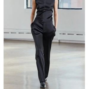 Svarta glansiga byxor med sömmar - Elegant svara byxor med finna sömmar som en detalj. Den har en figurnära passform upptill och vida ben. Perfekt för en stilren look. Helt nya med prislapp💗 nypris 700kr