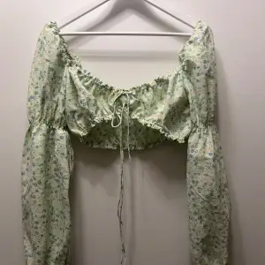 Blommig blus i ljusgrön med små blommor i rosa och blått. Blusen har långa ärmar och en söt knytning framtill. Perfekt för en somrig look 💖