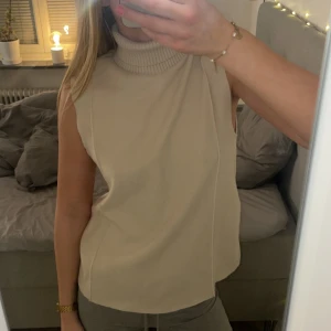 Beige ärmlös polotröja från Zara - Jag säljer min jättefina kortärmade stickad topp med hög krage från Zara. Tröjan är i storlek S och är aldrig använd!💕