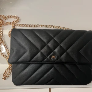 Svart axelväska med guldkedja - Snygg svart axelväska med quiltad design och elegant guldkedja. Perfekt för att ge en stilren touch till din outfit. Väskan har en praktisk storlek och en diskret logga framtill.💕