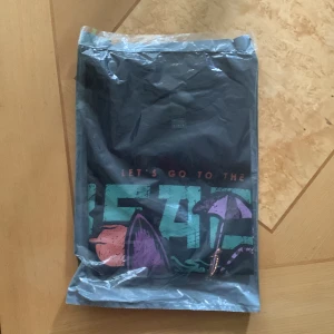 Kortärmad tröja - Medium oanvänd  - Detta är en kortärmad tröja med tryck i storlek M. Gjord av 100% bomull och har aldrig använts. På trucket står det ”LET’S GO TO THE BEACH” i olika färger. Köpt från EMP.
