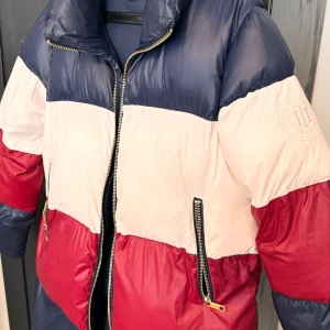 Flerfärgad pufferjacka från Tommy Hilfiger - Säljer en snygg och varm pufferjacka från Tommy Hilfiger. Jackan är flerfärgad med blå, vit och röd sektioner. Den har en dragkedja framtill och två fickor med dragkedjor. Perfekt för kalla dagar! 🧥