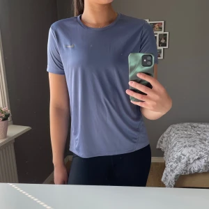 Tränings-t-shirt från Nike - Säljer en lila tränings-t-shirt från Nike. Använd ett fåtal gånger, men har lite små defekter pga tvättmaskin (se bild 4-5), men inget som syns jätte tydligt! 