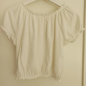 Vit kortärmad topp från KappAhl - Säljer en söt vit topp från Kappahl. Den har korta ärmar och en elastisk halsringning som gör att den kan bäras off-shoulder. Den har en avslappnad passform och är superbekväm att ha på sig. Perfekt för både vardag och fest! Storlek 146/152, passar även mig som bär XS. Använd fåtal gånger, mycket bra skick. 