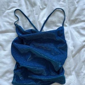 Blå glittrig linne - Säljer en snygg blå glittrig linne med smala axelband. Perfekt för festliga tillfällen! Linnet är i ett stretchigt material som sitter tight och bekvämt. Passar bra till både jeans och kjol. Använd ett fåtal gånger, så det är i nyskick.
