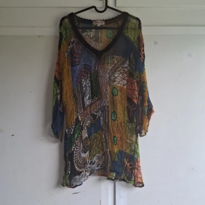 Färgglad blus från Indiska - Säljer en färgglad blus från Indiska i storlek XL. Blusen har ett unikt mönster i flera färger som blå, grön, gul och orange. Den har en v-ringad hals och trekvartsärmar. Perfekt för att liva upp garderoben!