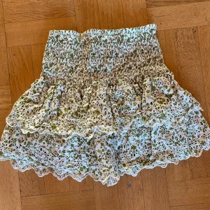 Blommig kjol från Zara - Superfin blommig kjol från Zara i storlek L men sitter mer som S, därav markeringen. På bilden är den lagd på ett par jeans med storlek W28. Den har ett elastiskt midjeband som gör den bekväm och lätt att bära. Kjolen är kort och har ett vackert blommönster i grönt och vitt. Den är perfekt för sommardagar och har fina volangdetaljer som ger en söt touch💓