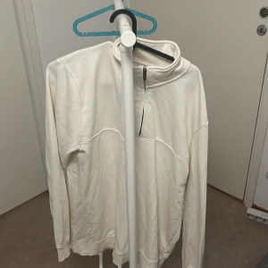 Vit tröja med dragkedja från Dressmann - Säljer en stilren vit tröja från Dressmann i storlek L. Tröjan har en praktisk dragkedja vid halsen och är långärmad. Perfekt för en avslappnad stil eller som ett extra lager under kalla dagar.