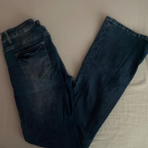 Mörkblå jeans - Säljer ett par snygga mörkblå jeans. De har en klassisk femficksdesign och en knappgylf. Perfekta för vardagsbruk och kan matchas med nästan vad som helst. Passformen är lågmidjade och de är i bra skick.