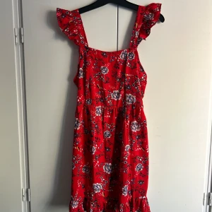 Röd blommig klänning från Boohoo - Säljer en superfin röd klänning från Boohoo med blommigt mönster. Den har volangdetaljer vid axlarna. Klänningen är i nyskick och har fortfarande etiketten kvar. 🌸