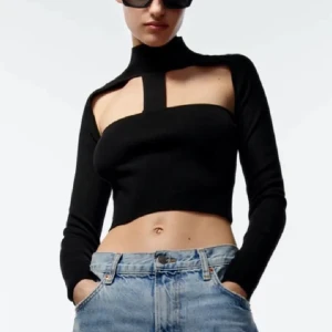 Svart croppad topp med hög krage - Säljer denna ursnygga topp med hög krage och unikt cutout mönster eftersom den aldrig har kommit till användning sen jag köpte den. Perfekt för en utekväll eller fest! Den har långa ärmar och en tight passform som framhäver figuren. Toppen har endast ett streck där fram, men är öppen i ryggen. 