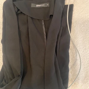 Svart kavaj från Gina Tricot - Säljer en stilren svart kavaj från Gina Tricot i storlek 34. Perfekt för både vardag och fest! Kavajen har en enkel design utan knappar och är långärmad. Passar bra till jeans eller klänning för en chic look.