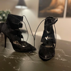 Svarta klackskor med snörning - Snygga svarta klackskor i mocka med spetsig tå och elegant snörning. Perfekta för en utekväll eller fest. De har en hög klack som ger en stilren look. Skorna är i bra skick och redo att användas för att lyfta din outfit.