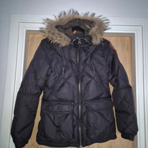 Parajumpers jacka i storlek S  - Svart jacka med huva med avtagbar pälskrage samt flera fickor. Den är använd och i mycket fin skick. Inga skador.  En svag synligt fläck av klistermärken finns på insidan(bild 5).Den syns mer på bilden än i verkligheten.  Färg: svart  Storlek: small