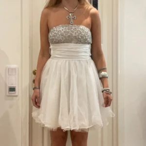 Studentklänningen  - Elegant vit axelbandslös klänning med glittrig paljettöverdel och volangkjol. Perfekt för festliga tillfällen eller studenten. Så fin hade på min student och sen var suverän