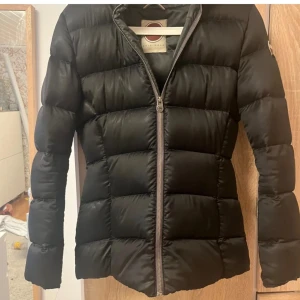 Svart dunjacka från Colmar - Snygg svart dunjacka från Colmar med dragkedja och huva.. Den är figurr sydd. Har ett hål innanför dragkedjan som du ser på näst sista bilden men har efter mitt köp lappat den som du ser på sista bilden! Är i bra skick. Skriv vid frågor!🩷 Har använt ca 4 gånger.🩷🩷 Nypris: 4799