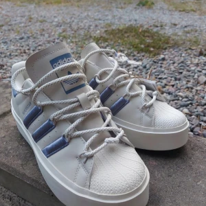 Adidas Superstar sneakers - Snygga Adidas Superstar sneakers i vitt med lila detaljer. Perfekta för en stilren look. Helt nya! Storlek 36 (de är väldigt små i storleken). 