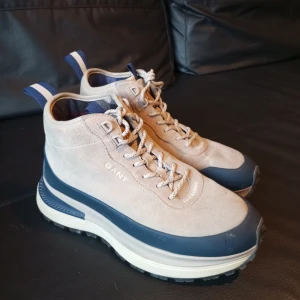 Beige sneakers från GANT - Snygga sneakers från GANT i beige mocka med blå detaljer. Skorna har en tjock sula och märket synligt på sidan och bak. Använda fåtal gånger Nypris 1800:-