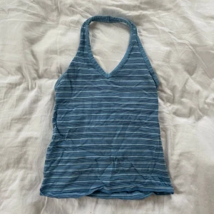 Blå randig halterneck-linnetopp - Snygg blå randig halterneck-linnetopp med smala axelband och v-ringning. Perfekt för sommardagar och ger en avslappnad look. Står ingen storlek men uppskattas vara en S. 