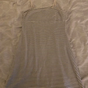 Randig ärmlös klänning - Snygg och enkel randig klänning med smala axelband. Perfekt för en avslappnad dag. Klänningen har en klassisk design med tunna ränder i svart och vitt.