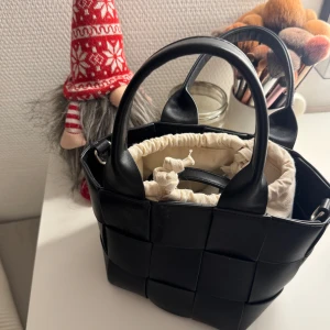 Flätad väska!! - Snygg svart handväska med quiltad design och praktiskt innerfoder i beige. Väskan har två handtag och en dragkedja för säker förvaring. Perfekt för att ge en stilren touch till din outfit.