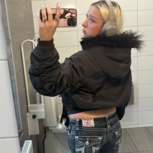 Svart bomberjacka med pälskrage - Snygg svart bomberjacka med fluffig pälskrage och huva. Jackan är croppad och har dragkedja framtill. SLUTSÅLD på weekday 