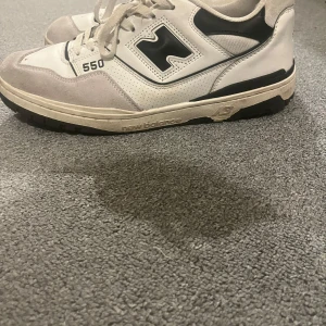 New Balance 550 sneakers - Snygga New Balance 550 sneakers i vitt och svart med grå detaljer. Skorna har snörning och en klassisk design med märkets logga på sidan och hälen. Perfekta för en stilren look.