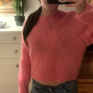 Rosa stickad tröja - Säljer en söt rosa stickad tröja med croppad passform. Tröjan har långa ärmar och en rund halsringning, perfekt för en mysig look. Passar bra till jeans eller kjol för en avslappnad stil.
