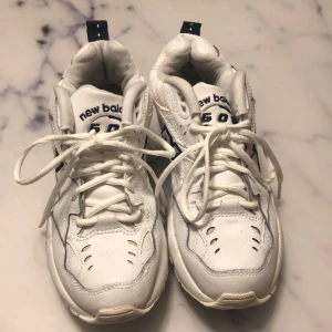 Vita sneakers från New Balance - Snygga vita New Balance 608 sneakers med blå detaljer och snörning. Perfekta för en sportig look med bekväm passform och slitstark sula. Används 1-2 gånger 