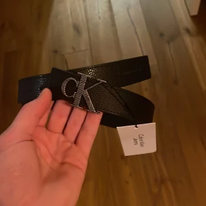 Svart bälte från Calvin Klein Jeans - Snyggt svart bälte från Calvin Klein Jeans med en stilren CK-logga i silver på spännet. Perfekt för att ge en elegant touch till din outfit. helt oanvänd.