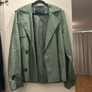 Grön trenchcoat från Vero Moda - Snygg grön trenchcoat från Vero Moda med knappar framtill och på ärmarna. Jackan är perfekt för våren och hösten. 