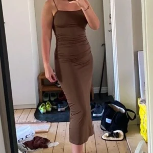 Brun axelband klänning - Snygg brun axelbandslös klänning med slits på sidan. Klänningen har en tight passform och är perfekt för en elegant look.