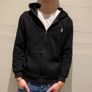 Ralph lauren hoodie - Snygg svart hoodie från Polo Ralph Lauren med dragkedja och klassisk logga på bröstet. Perfekt för en avslappnad stil. Den har långa ärmar och en bekväm huva. Den är i storlek M och modellen är 180cm lång. Den är i princip nyskick och originalpåse medföljer. Vid funderingar eller frågor är det bara att höra av sig🙌 pris går alltid att diskutera!