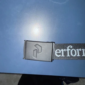 Svart bälte - Snyggt svart bälte från Peak Performance med vit text. Längden är 100cm så passar utmärkt till både vuxna och barn. Bältet har en stilren design med ett spänne i svart. Perfekt för att ge en sportig touch till din outfit.