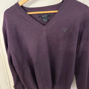 Lila tröja i merinoull från GANT - Säljer en stilren lila tröja från GANT i extrafin merinoull. Tröjan har en v-ringad design och långa ärmar, perfekt för kyligare dagar. Den är mjuk och bekväm, idealisk för både vardag och mer uppklädda tillfällen.