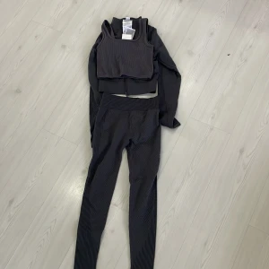 Svart träningsset med ribbade detaljer - Snyggt grått träningsset med ribbade detaljer. Setet inkluderar en ärmlös topp och matchande leggings. Perfekt för träning och bekvämt att bära. Allt tillsammans för 180. Bara byxor 40 , bara toppen 30 och koftan 40