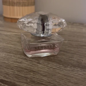 Versace Bright Crystal parfym - Elegant parfymflaska från Versace med en stor, kristalliknande kork. Flaskan är genomskinlig med en rosa tonad vätska inuti. Perfekt för den som älskar lyxiga och sofistikerade dofter. 50ml finns cirka halva kvar 