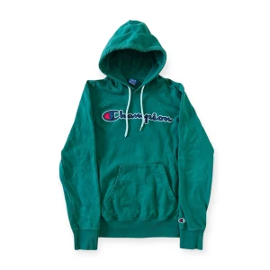 Grön hoodie från Champion - Säljer en snygg grön hoodie från Champion med klassisk logga på bröstet. Tröjan har en liten fläck på framsidan (se bild), har försökt ta bort med fall tvål men lyckades inte. Annars i fint skick! Passar som en S.