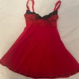 Coqette röd nattlinne med spetsdetaljer - Snyggt rött nattlinne med svarta spetsdetaljer och rosett framtill. Axelbandslös design med justerbara band för perfekt passform. Det står storlek S/M på lappen.