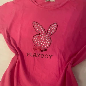 Rosa t-shirt med Playboy-logga - Snygg rosa t-shirt med glittrande Playboy-logga framtill. Lappen är lite suddig så vet inte vilket märke det egentligen är, och det står inte heller någon storlek men baserat på mig som är storlek S skulle jag gissa på att den är xs-s