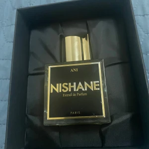 Nishane Ani Extrait de Parfum - Säljer en exklusiv Nishane Ani Extrait de Parfum. Flaskan är elegant med en fyrkantig form och en gyllene kork. Parfymen har en djup gul färg och kommer i en stilren svart förpackning med gyllene detaljer. Perfekt för den som söker en lyxig doftupplevelse. Mängd enligt bild (60-65ml ungefär)🙌🏼 nypris på 50ml:1900 min 60-65:1400